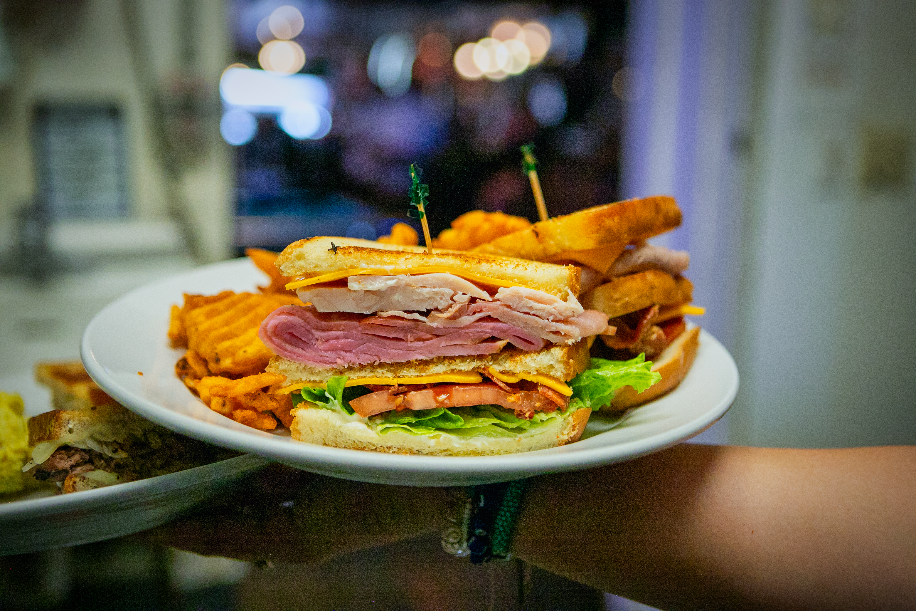 A triple decker sandwich of turkey, ham and bacon, with a side of fries and pickle
