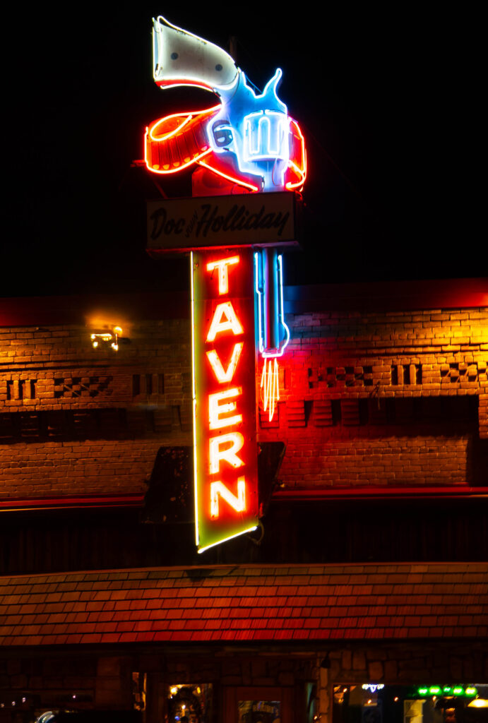 A western neon sign of a pistol at nighttime glows in it red and blue neon.