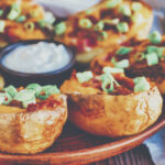 Baked loaded potato skins with cheddar cheese and bacon, garnished with scallions and sour cream, horizontal
