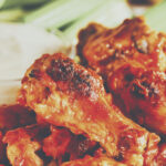 A plate with hot spicy wings with dressing and celery in the background